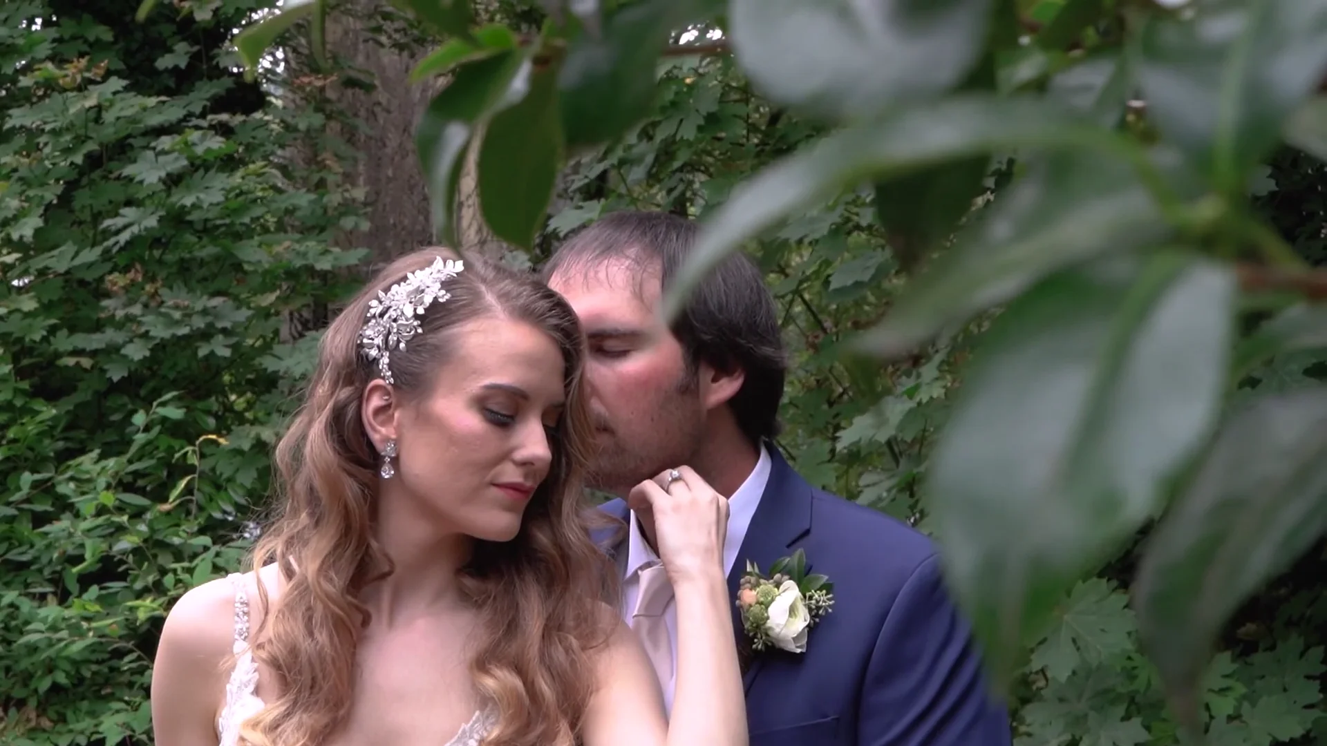 Video still of the groom kissing the bride’s cheek among the garden greenery