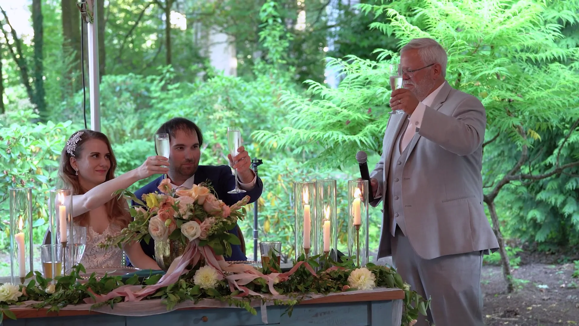 Video still of the father of the bride giving a toast beside the couple